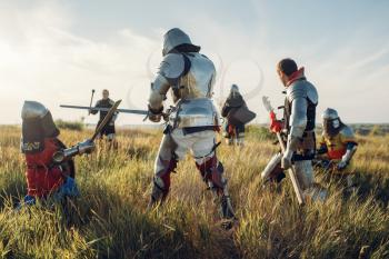 Medieval knights in armor and helmets fight with sword and axe. Armored ancient warrior in armour posing in the field