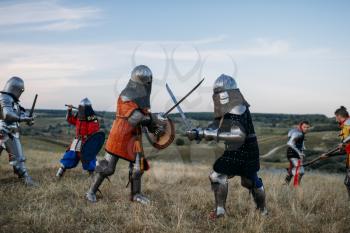Medieval knights in armour and helmets fight with swords. Armored ancient warriors posing in the field