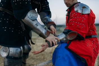 Medieval knight helps his friend to put on armor, great tournament. Armored ancient warrior in armour posing in the field