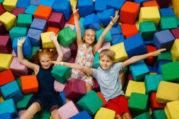 Happy children lying in soft cubes, playground in entertainment center. Play area indoors, playroom