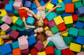 Happy children lying in soft cubes, playground in entertainment center. Play area indoors, play room