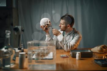 Male psychiatrist in lab coat examines the human skull, mental hospital. Doctor in clinic for the mentally ill