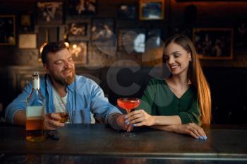 Couple with alcohol gets acquainted at the counter in bar. Man and woman celebrate the meeting in pub, human emotions, leisure activities, flirting