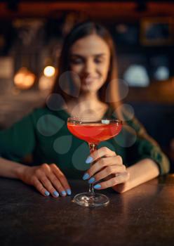 Smiling woman drinks coctail at the counter in bar. One female person in pub, human emotions, leisure activities, nightlife