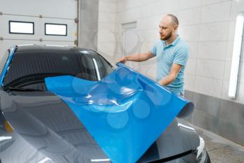 Male car wrapper holds protective vinyl foil or film roll. Worker makes auto detailing. Automobile paint protection coating, professional tuning