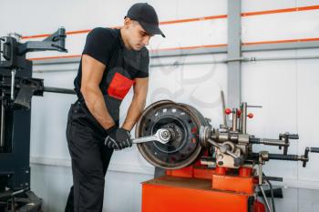 Mechanic repairs a crumpled disc, tire repairing service. Man fixing car tyre in garage, professional automobile inspection in workshop