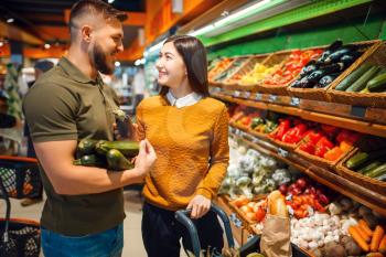 Happy couple with basket in grocery store together. Man and woman buying fruits and vegetables in market, customers shopping