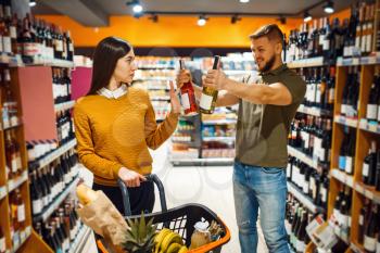 Cheerful couple choosing alcohol in supermarket. Man and woman buying beverages in market, customers shopping food and drinks