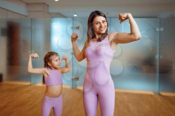 Mother and daughter shows the muscles in gym, healthy lifestyle, fitness workout. Mom and little girl in sportswear, woman with kid on joint training in sport club
