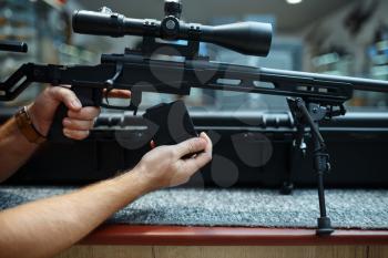 Male person loads sniper rifle in gun shop. Euqipment for hunters on stand in weapon store, hunting and sport shooting hobby