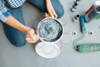 Female house painter mixes black and green paints in pail, closeup. Home repair, laughing woman doing appartment renovation, room decoration renovating