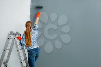 Female house painter paints walls indoor. Home repair, laughing woman doing appartment renovation, room decoration renovating