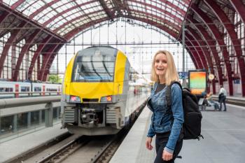 Female tourist with backpack waiting for train on railway station platform, travel in Europe. Transportation by european railroads