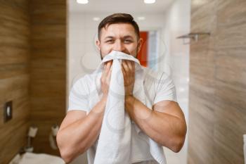 Man wipes his face with a towel, front view, routine morning hygiene. Male person at the sink performs skin and body treatment procedures