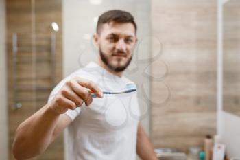 Man brushes his teeth in bathroom, front view on face, routine morning hygiene. Male person at the sink performs skin and body treatment procedures