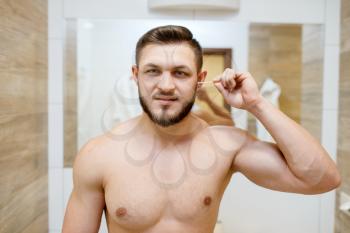 Man cleans his ears with cotton swabs, morning routine hygiene procedures. Athletic male person at the mirror in bathroom