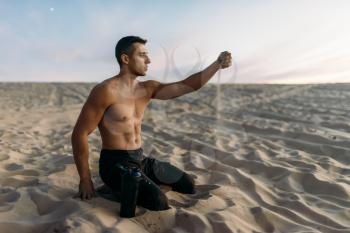 Sportsman sitting on sand after workout in desert at sunny day. Strong motivation in sport, strength outdoor training
