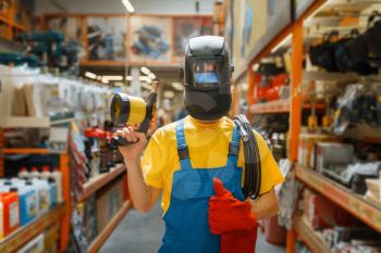 Male builder choosing welding equipment at the shelf in hardware store. Constructor in uniform look at the goods in diy shop