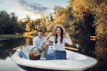 Love couple with fruit basket in boat on quiet lake at summer day. Romantic date, boating trip, man and woman walking along the river
