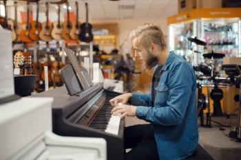 Male musician trying to play on piano in music store. Assortment in musical instruments shop, keyboardist buying equipment, pianist in market