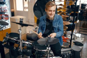 Bearded young musician plays on drum set in music store. Assortment in musical instrument shop, professional equipment for performers