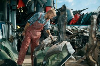 Dirty male repairman choosing spare parts on car junkyard. Auto scrap, vehicle junk, automobile garbage, abandoned, damaged and crushed transport