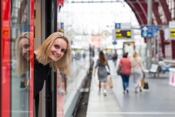 Female tourist looks out of the train on railway station platform, travel in Europe. Transportation by european railroads, comfortable tourism and travelling