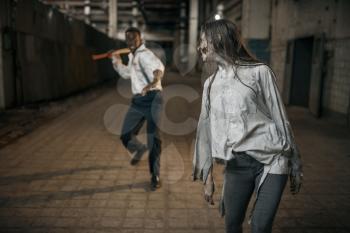 Man with axe attacked female zombie in abandoned factory, scary place. Horror in city, creepy crawlies, doomsday apocalypse, bloody evil monsters