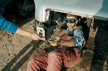 Male mechanic in welding glasses on car junkyard. Auto scrap, vehicle junk, automobile garbage. Abandoned, damaged and crushed transport, scrapyard