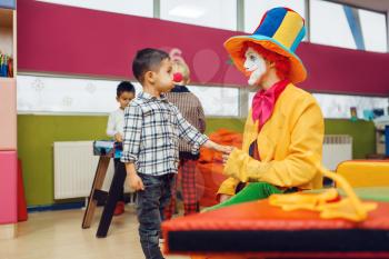 Funny clown and little boy with red nose are playing together. Birthday party in playroom, baby holiday in playground. Childhood happiness, childish leisure