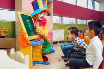 Funny clown with happy children play in the alphabet on board. Birthday party celebrating in playroom, baby holiday in playground. Childhood happiness, childish leisure