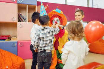 Funny clown with cheerful children play counting game together. Birthday party celebrating in playroom, baby holiday in playground. Childhood happiness, childish leisure