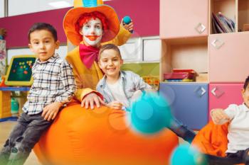 Funny clown with little boy in kindergarten. Birthday celebrating in playroom, baby holiday in playground. Childhood happiness, childish leisure