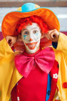 Funny clown with makeup dressed in colorful hat and costume poses in children's area. Birthday party in playroom, baby holiday in playground. Childish leisure
