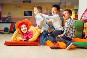 Joyful little boys sitting on funny clown in children's area. Birthday party celebrating in playroom, baby holiday in playground. Childhood happiness, childish leisure