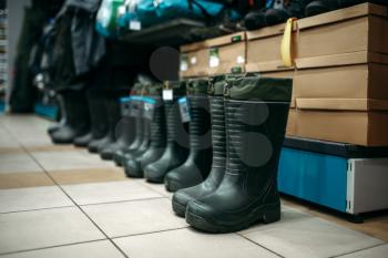Row of rubber boots in fishing shop, nobody. Equipment and tools for fish catching and hunting, accessory choice on showcase in store