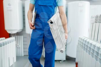 Plumber in uniform holds water heating radiator in plumbering store. Man buying sanitary engineering in shop