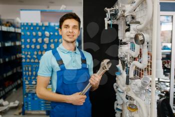 Plumber with pipe wrenches poses at the showcase, plumbering store choice. Man buying sanitary engineering tools and equipment in shop