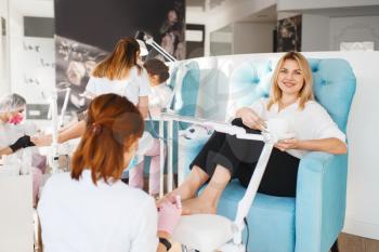Two women on pedicure procedure in beauty salon. Professional beauticians and female customers, toenail care in spa studio