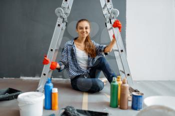 Cheerful female house painter sits on the floor. Home repair, happy woman doing appartment renovation, room decoration renovating