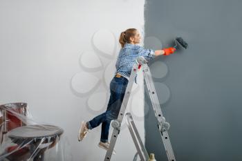 Female house painter in gloves paints the wall. Home repair, laughing woman doing appartment renovation, home renovation