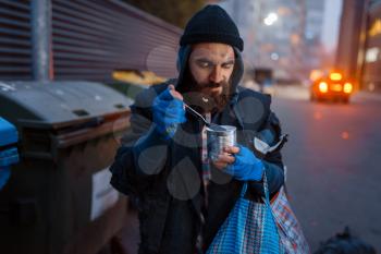 Homeless eating canned food on city street. Poverty is a social problem, homelessness and loneliness, alcoholism and drunk addiction, urban lonely