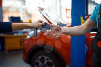 Female driver gives keys to worker in uniform, car service station. Automobile checking and inspection, professional diagnostics and repair