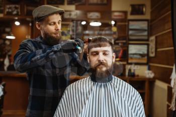 Barber with comb and scissors makes a haircut to a client. Professional barbershop is a trendy occupation. Male hairdresser and customer in retro style hair salon