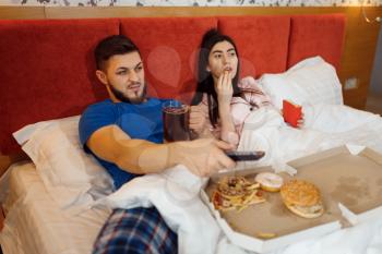 Couple eating in bed and watching TV, bad relationship, problems, family quarrel, conflict of married man and woman. Boring life of husband and wife