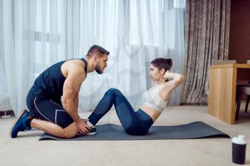 Morning fit training of couple at home. Active man and woman in sportswear doing exercise on the press in their house, healthy lifestyle, physical culture