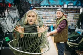 Fisherman catches woman in net, fishing shop, hooks and baubles on background. Equipment and tools for fish catching and hunting, accessory choice on showcase in store, bait assortment