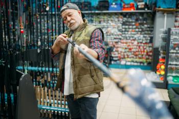 Male angler choosing rod in fishing shop. Equipment and tools for fish catching and hunting, accessory choice on showcase in store, spinnings and telescopes assortment