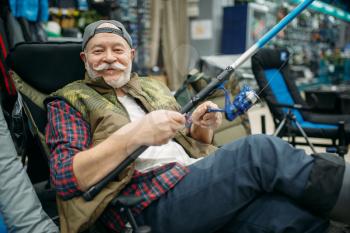 Male angler with rod sitting in chair, fishing shop. Equipment and tools for fish catching and hunting, accessory choice on showcase in store, spinnings and telescopes assortment