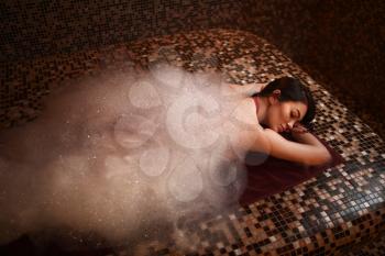 Woman in foam lying on a hot stone, turkish bath, hamam, sauna, top view. Skin and body care